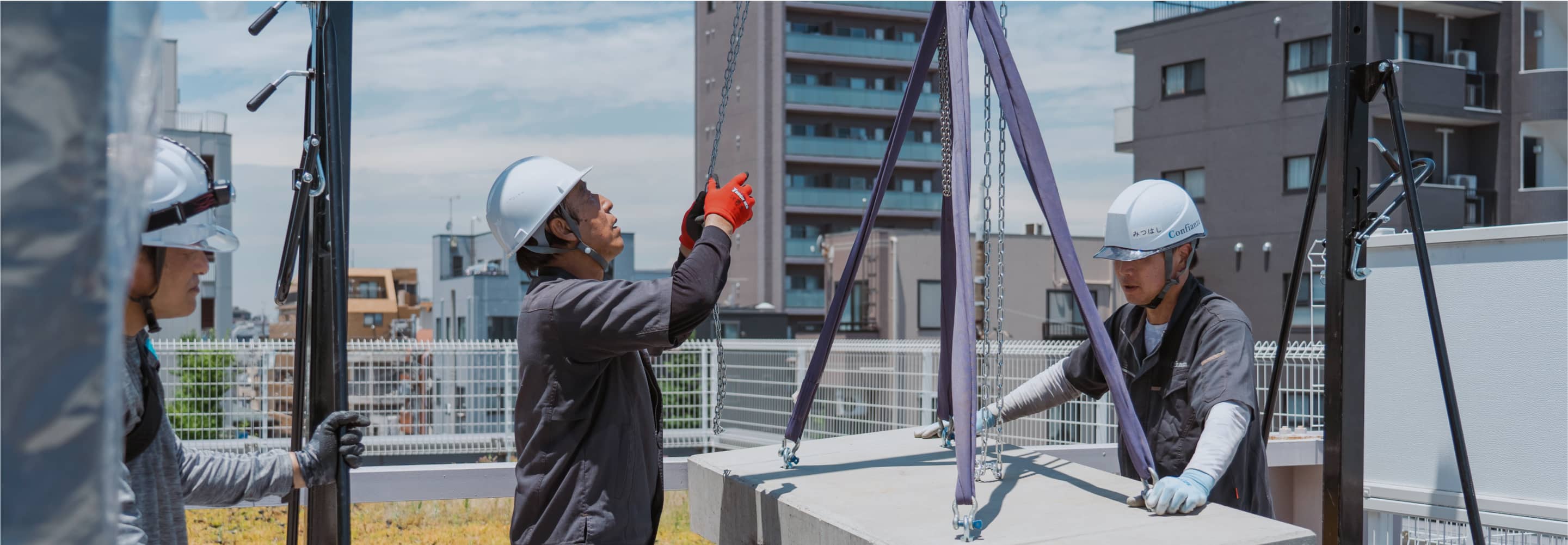 屋外で作業する作業員たちが、都市の景観を背景に見守る中、チェーンを調整している。