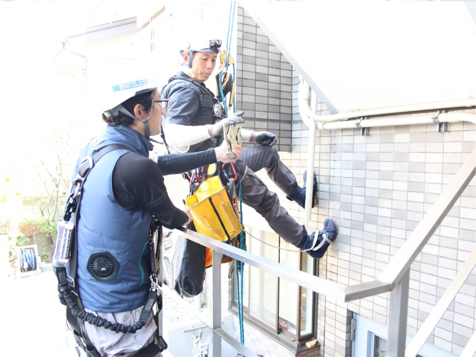 ロープとハーネスを使い、建物の壁で安全に作業を行う作業員たち。