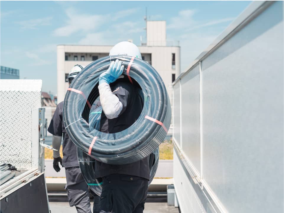 建物の屋上で、大きな巻きケーブルを肩に担いでいる作業員。