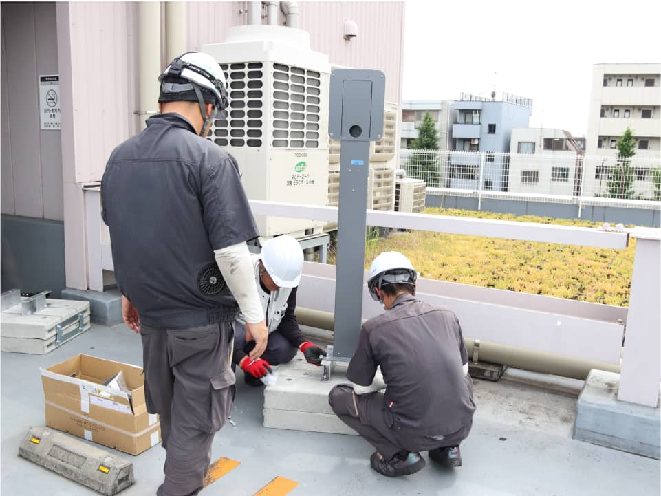 ヘルメットをかぶった作業員が、屋上で器具を設置している。