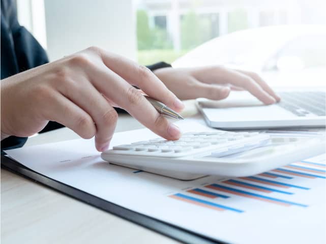 人が机で計算機を使用して財務報告書を分析している様子
