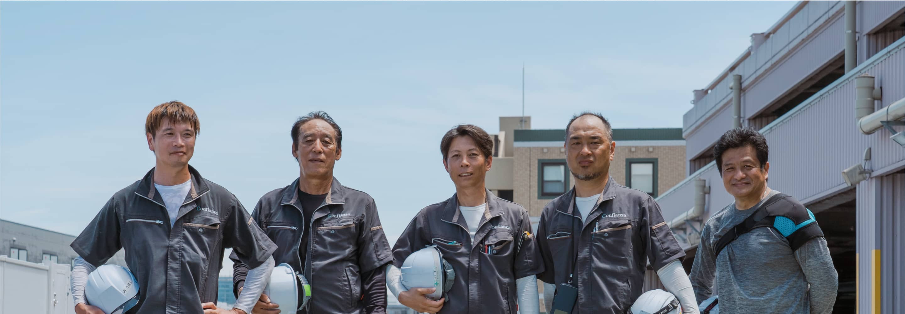 ヘルメットを手に持つ5人の建設作業員が一列に並んでいる。