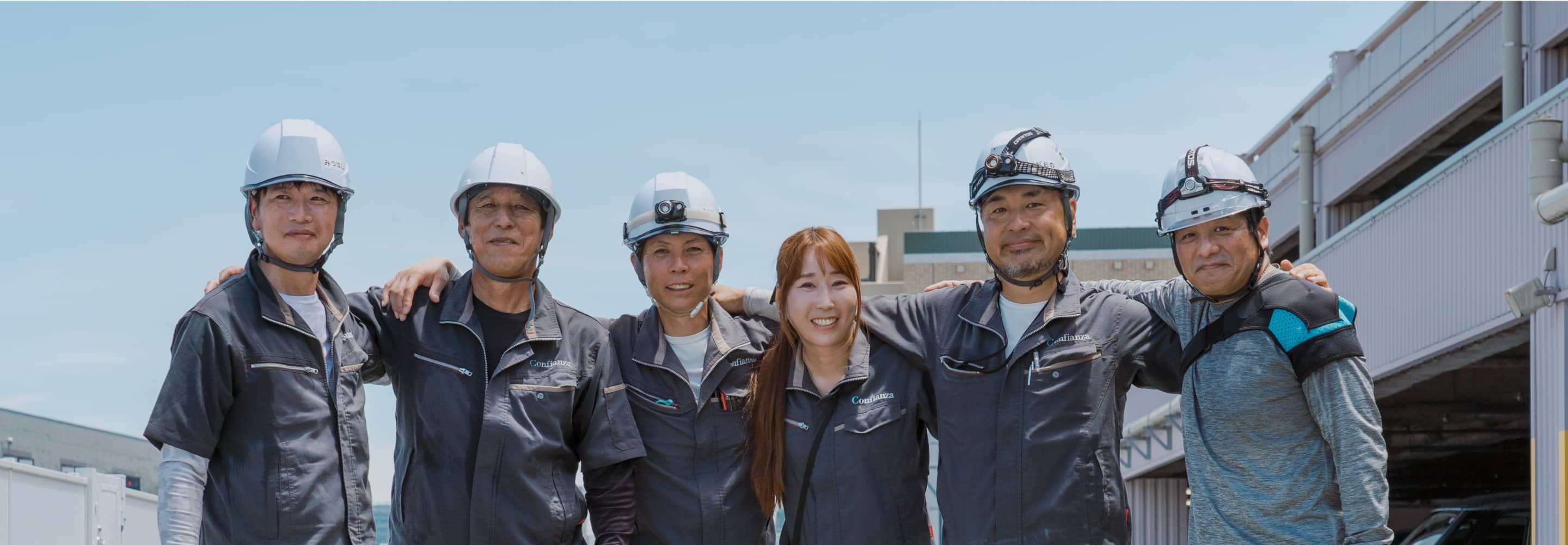 チームワークを示すように肩を組んでいる6人の作業員たち。